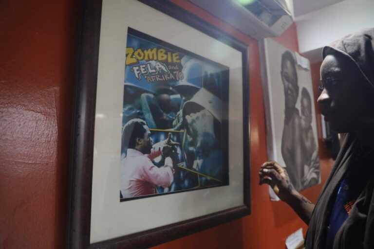 Qawiyat Omizi, a tour guide stand in front of a frame of Fela Kuti's Zombie at Kalakuta Museum in Lagos, Nigeria. Saturday, May 30, 2026. (AP Photo/Mansur Ibrahim)